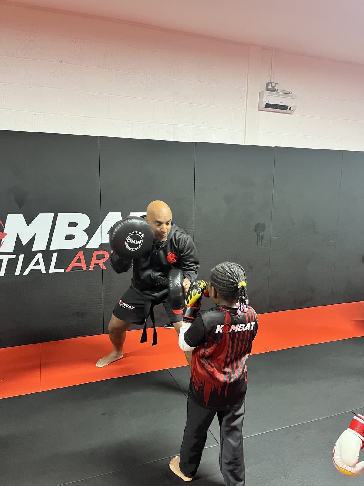 A Kombat coach holding pads for a young Kombat Cobras student